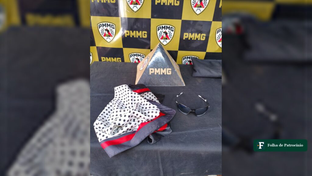 Óculos de sol e lenço apreendidos após furto em Patrocínio expostos sobre mesa com painel da PMMG ao fundo