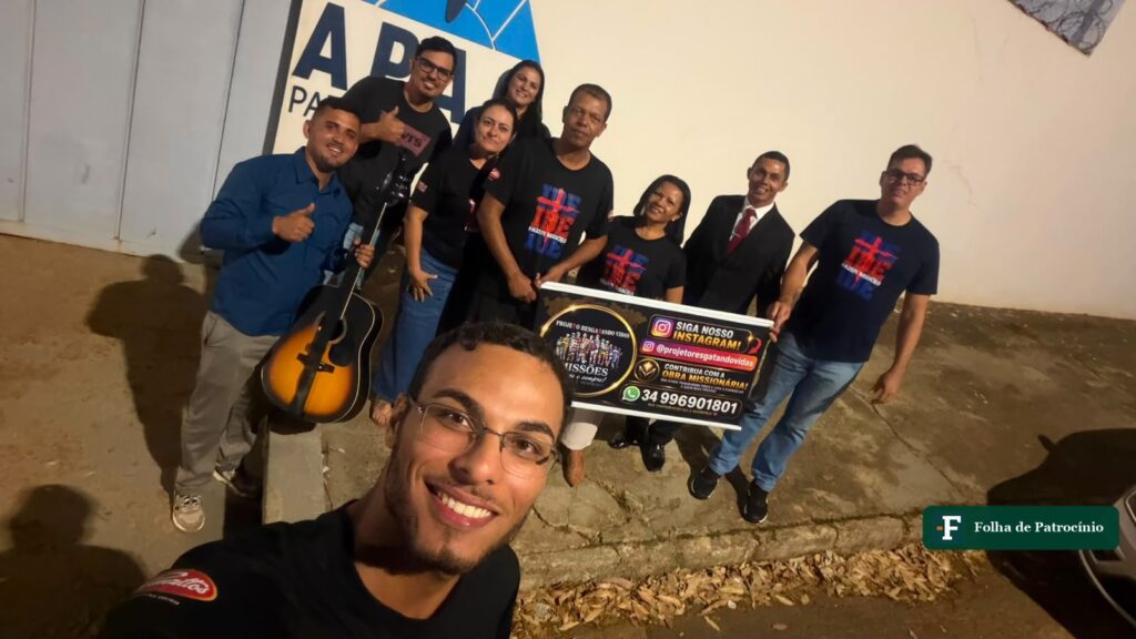 Voluntários do Projeto Resgatando Vidas em frente à APAC de Patos de Minas segurando o banner do grupo à noite