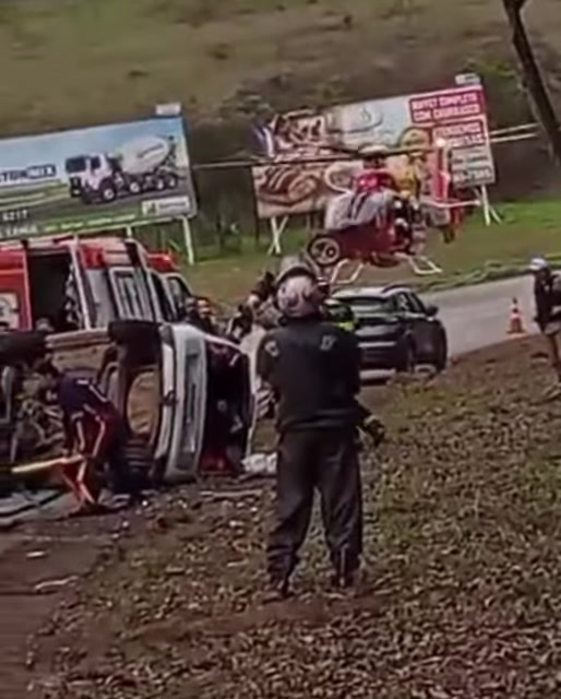 Helicóptero Arcanjo ao lado da pista e equipes de socorro junto a veículo tombado após o acidente na BR-356, em Itabirito