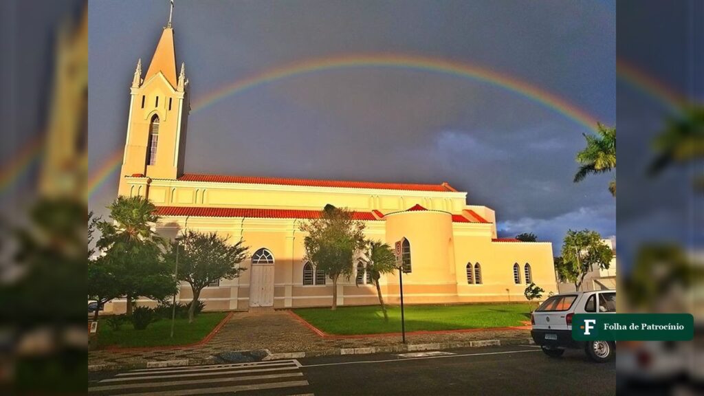 Igreja de Patrocínio sob céu carregado de tempestade e arco-íris, cenário dos alertas do Inmet para a semana. Foto: Acervo/@patrociniomg