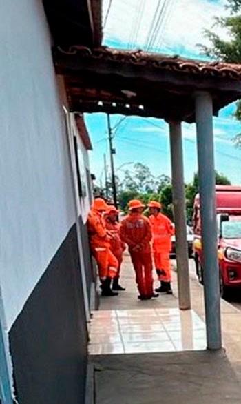 Bombeiros de farda laranja reunidos na calçada de uma casa durante as buscas pelo jovem desaparecido em Guimarânia