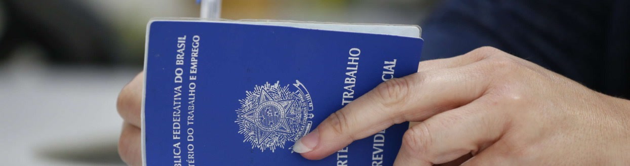 Mão segurando carteira de trabalho sobre uma mesa, documento exigido para as vagas em Patrocínio
