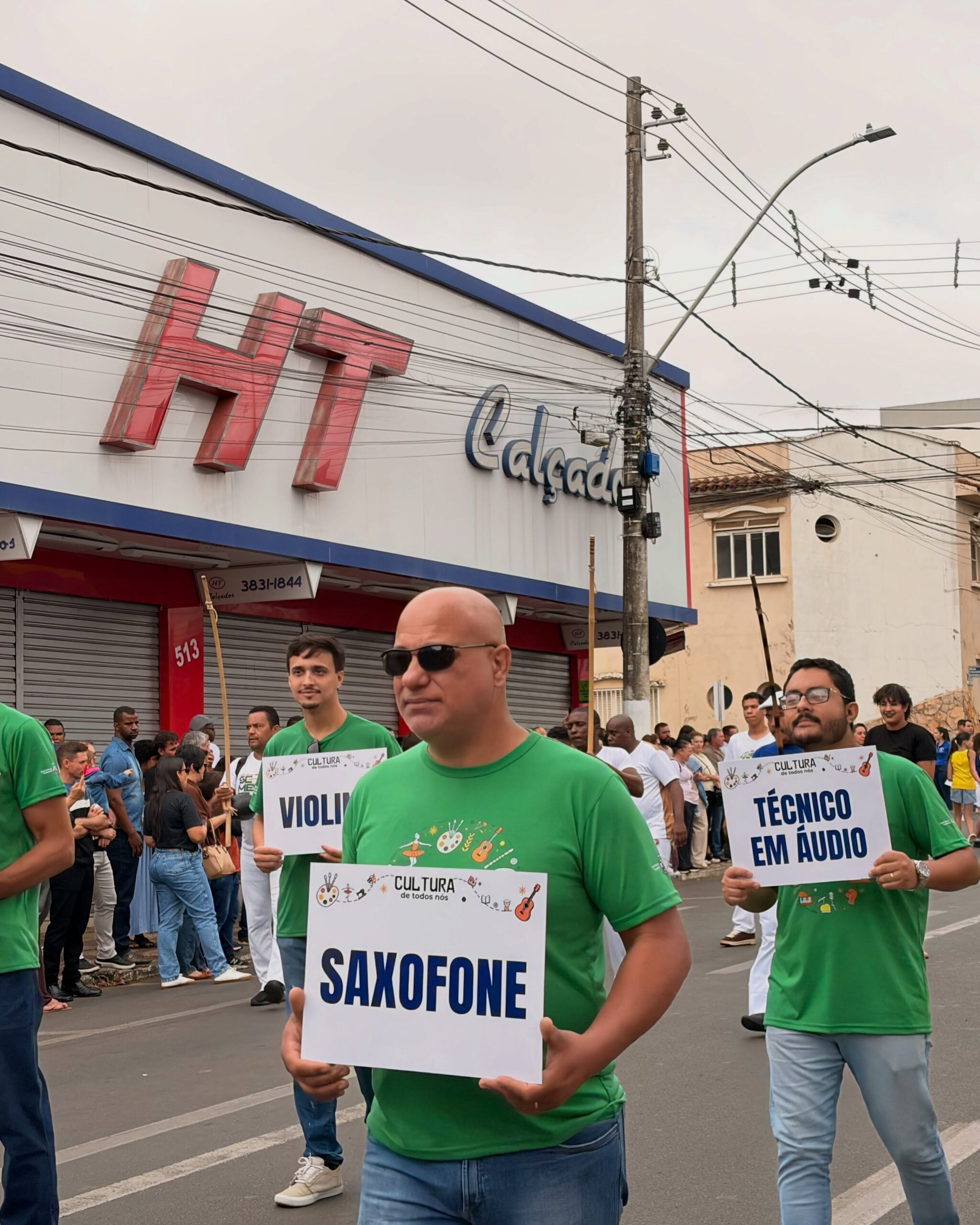 Pelotão da cultura no desfile cívico de Patrocínio caminha pela Avenida Rui Barbosa com placas das oficinas municipais