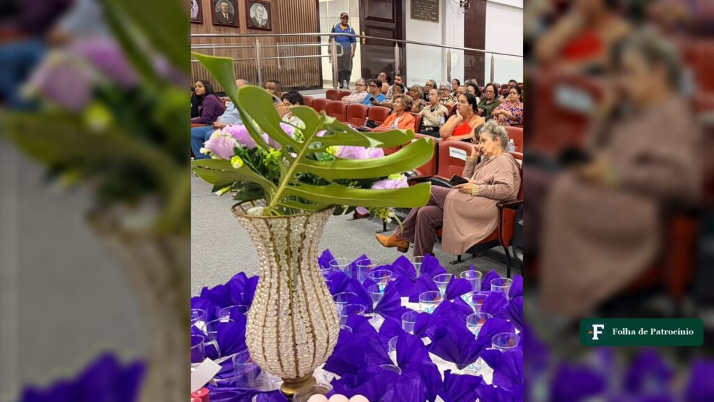 Idosas sentadas em auditório de poltronas vermelhas com arranjo de flores em primeiro plano, evento da pessoa idosa em Patrocínio, como o Dia do Idoso
