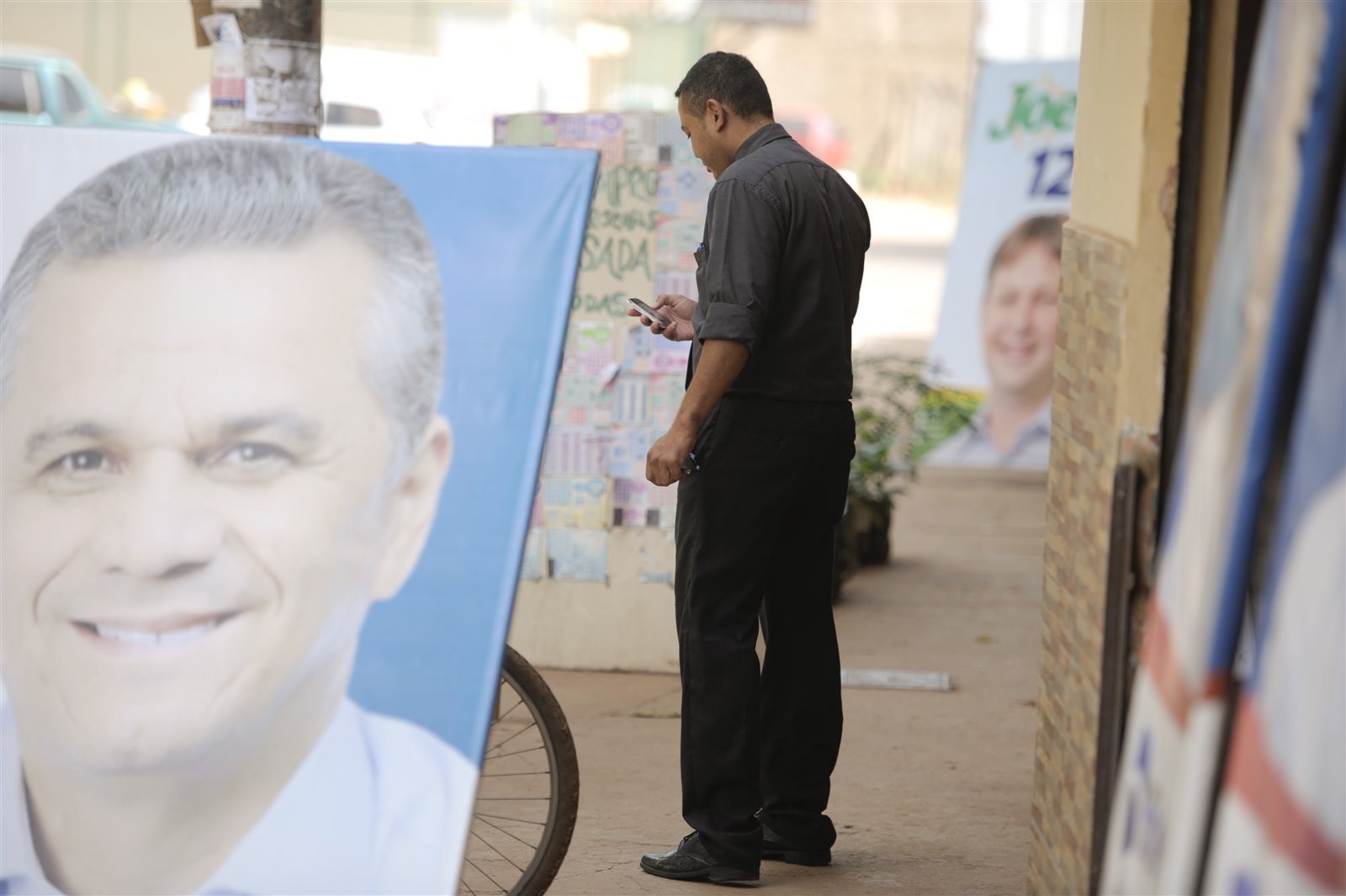 Bandeiras e placas de campanha apoiadas na calçada de uma rua comercial