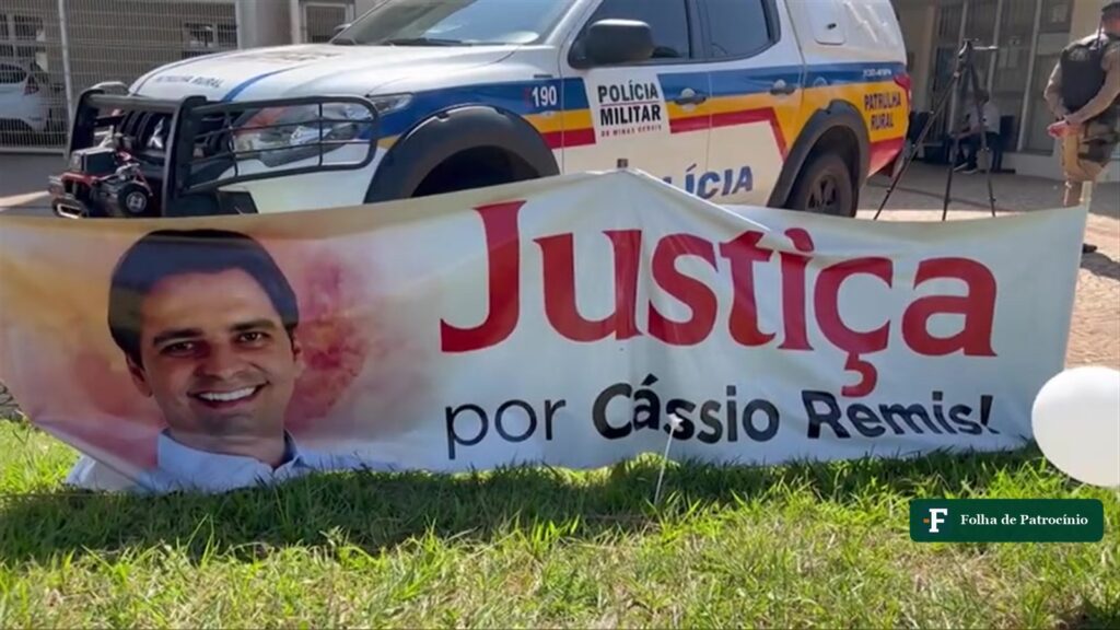 Faixa pede justiça pela morte de Cássio Remis em frente ao fórum, com viatura da Polícia Militar ao fundo