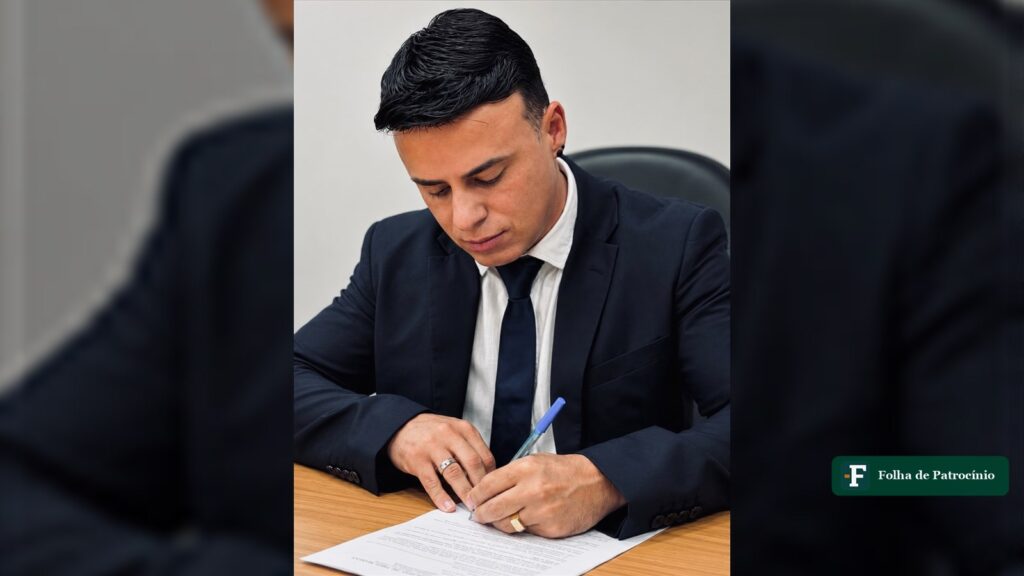 Prefeito de Três Marias, José Augusto, de terno escuro, assina o termo de posse em uma mesa