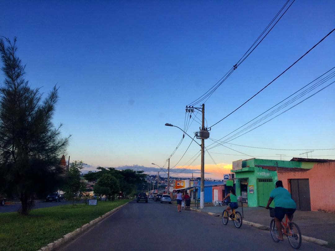 Rua de bairro em Patrocínio com comércio e ciclistas no fim de tarde, cidade com vagas no SINE nesta semana