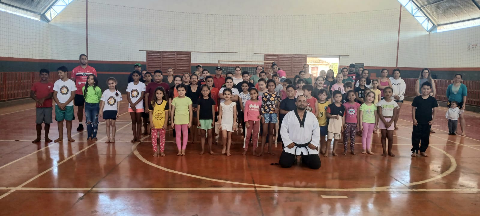Turma do Semeando Campeões reunida em ginásio com o professor Osmair Alves ajoelhado ao centro