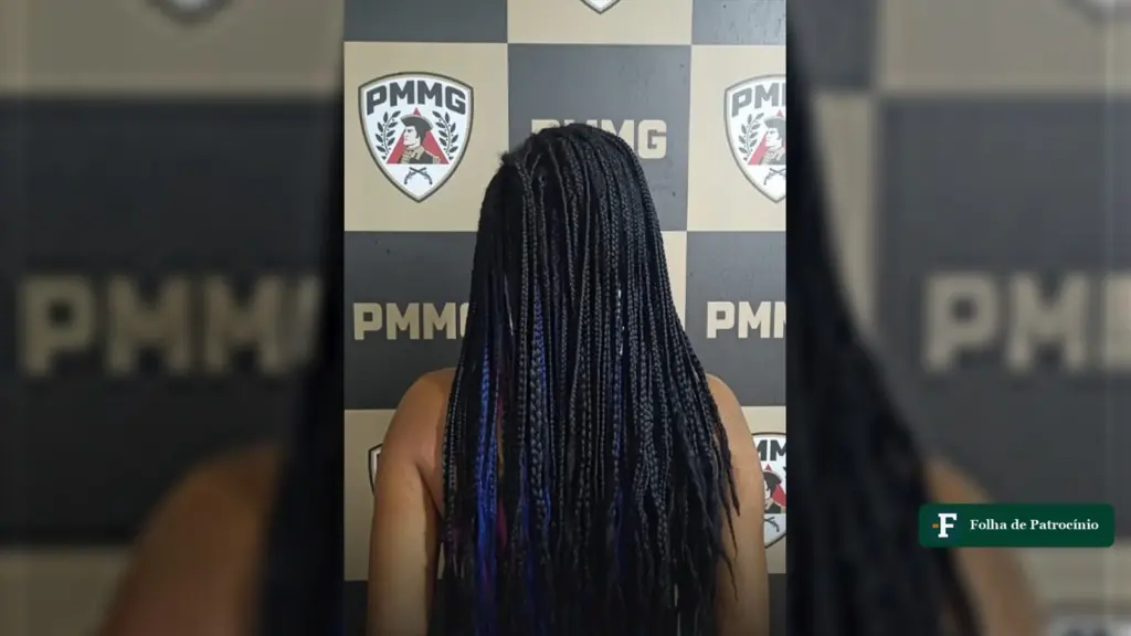 Mulher presa de costas diante do painel da Polícia Militar depois da agressão em João Pinheiro