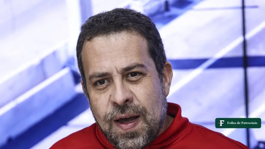 Guilherme Boulos gesticula ao falar em entrevista, de jaqueta vermelha do governo federal