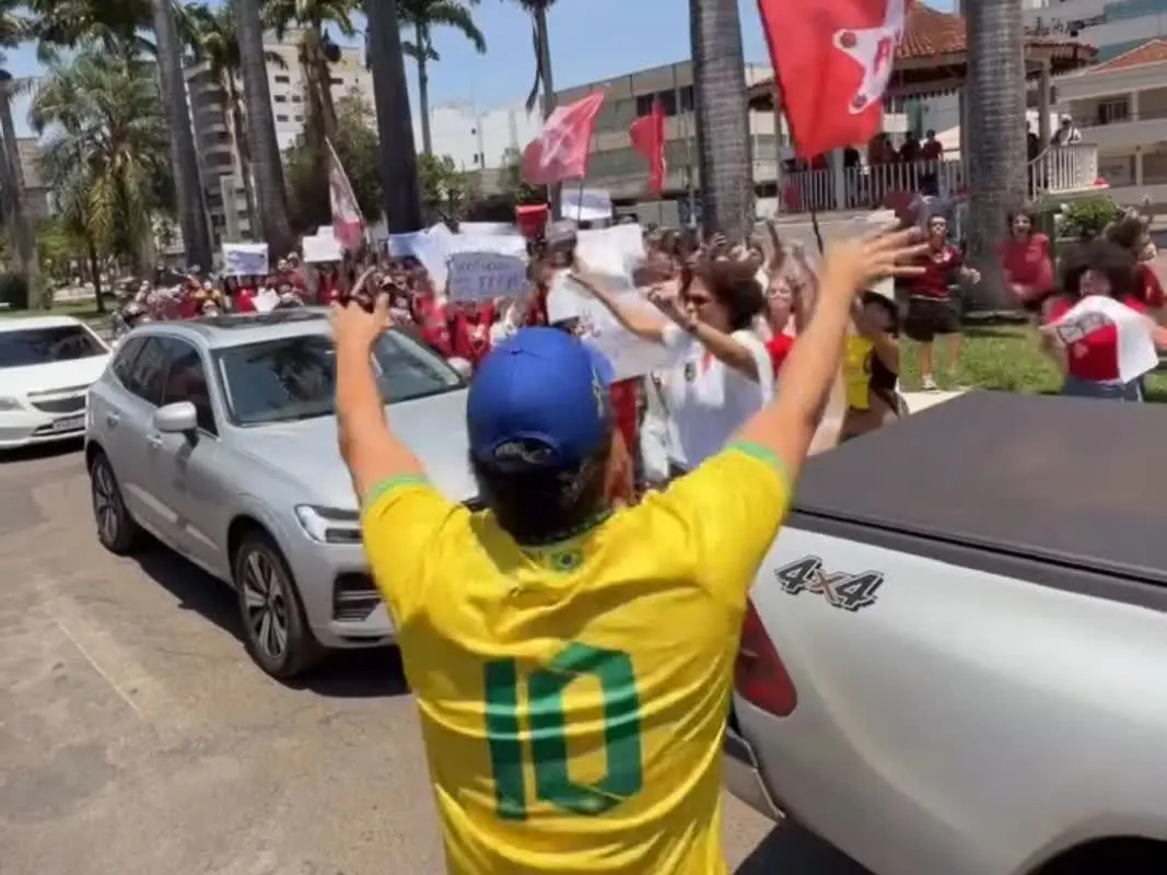 Homem de camisa amarela de costas diante de manifestantes com bandeiras vermelhas em Patos de Minas, no ato que gerou os ataques a manifestantes
