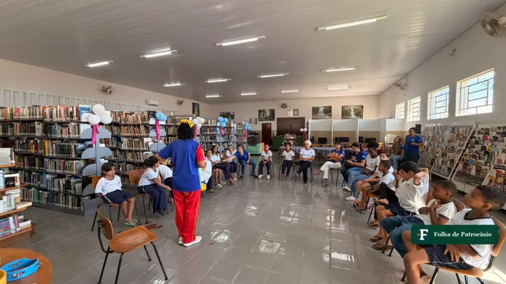 Contadora de histórias de pé diante de alunos sentados em roda no salão da Biblioteca Pública Municipal, durante a Aventura na Biblioteca
