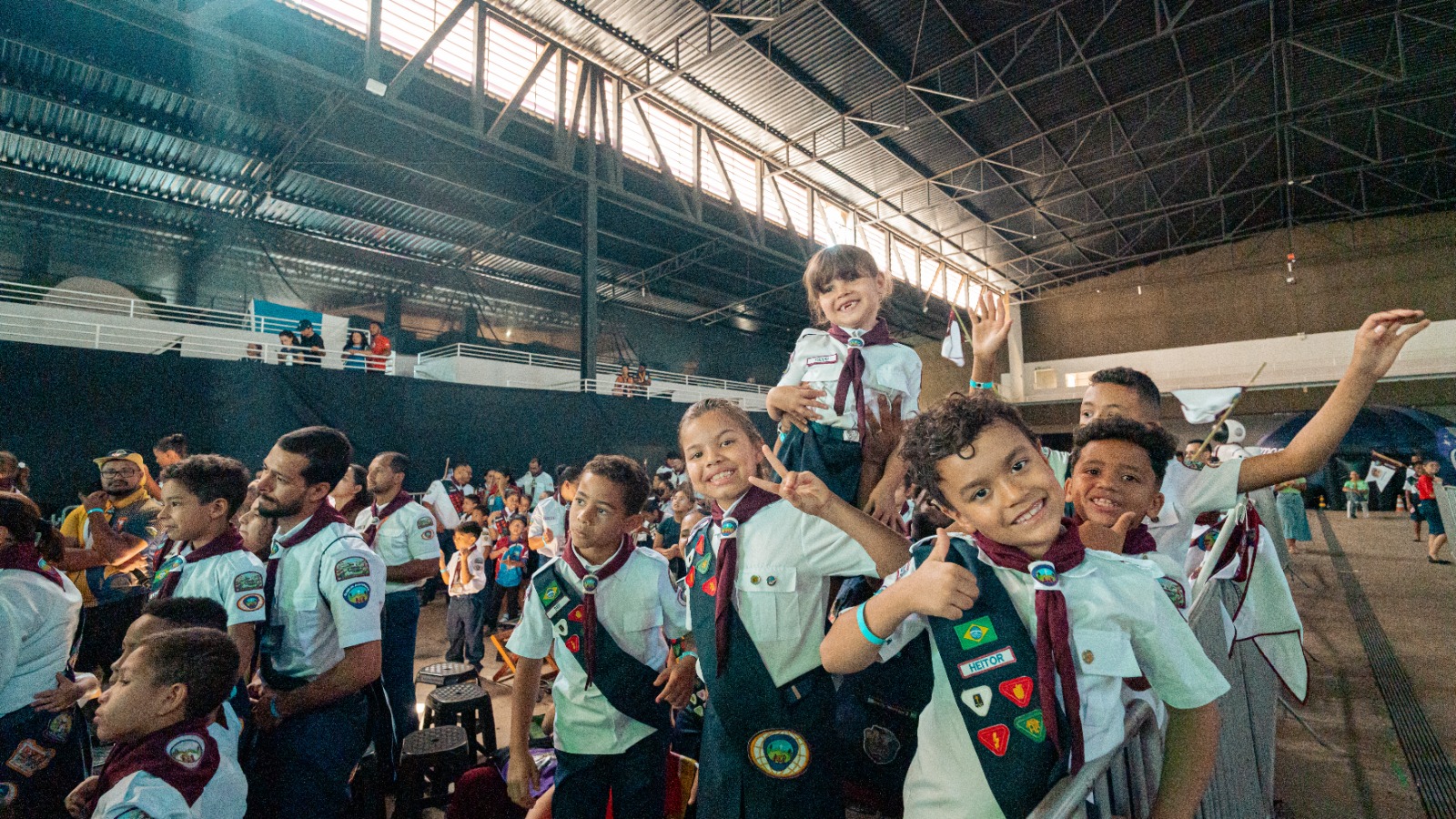Crianças uniformizadas na plateia, algumas com os braços erguidos
