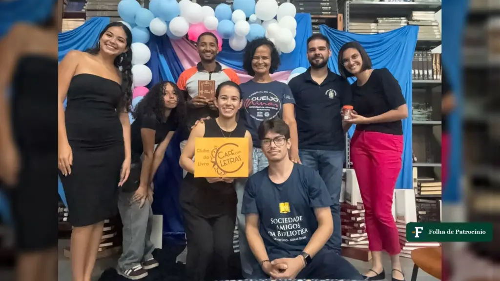 Participantes do Café com Letras posam com a placa do Clube do Livro na Biblioteca Pública Municipal de Patrocínio