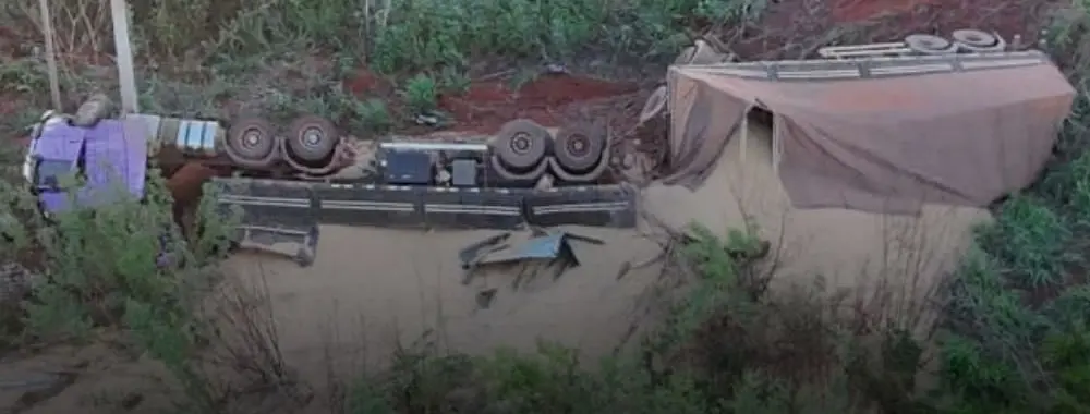 Detalhe da carreta em Uberlândia tombada na ribanceira, com a cabine roxa à esquerda e a carroceria coberta por lona