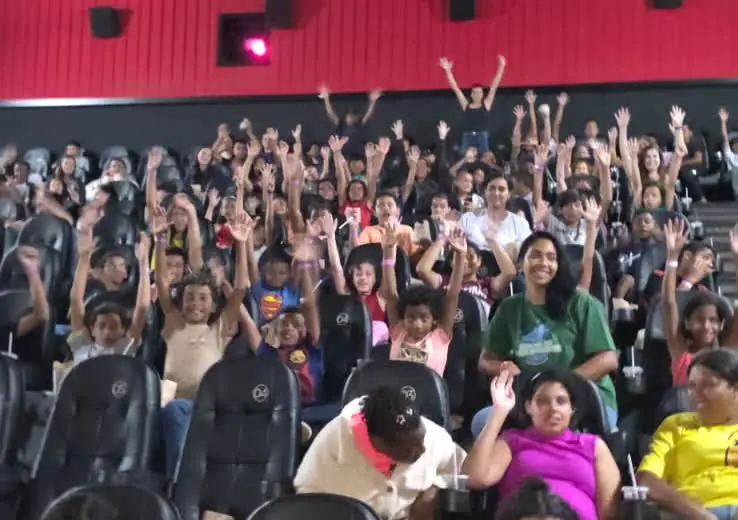 Plateia da sala do Patrocine com crianças de braços levantados durante o Cine Diversão em Patrocínio