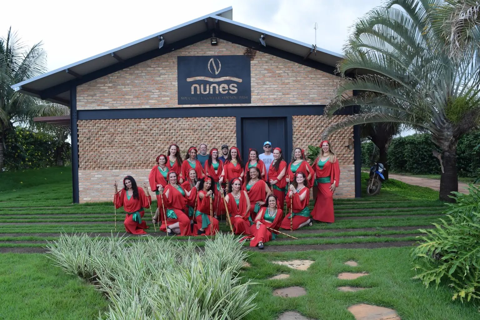 Mulheres do projeto Pátria, Terra e Grão, de vermelho e verde, posam diante do prédio de tijolos da Nunes Coffee