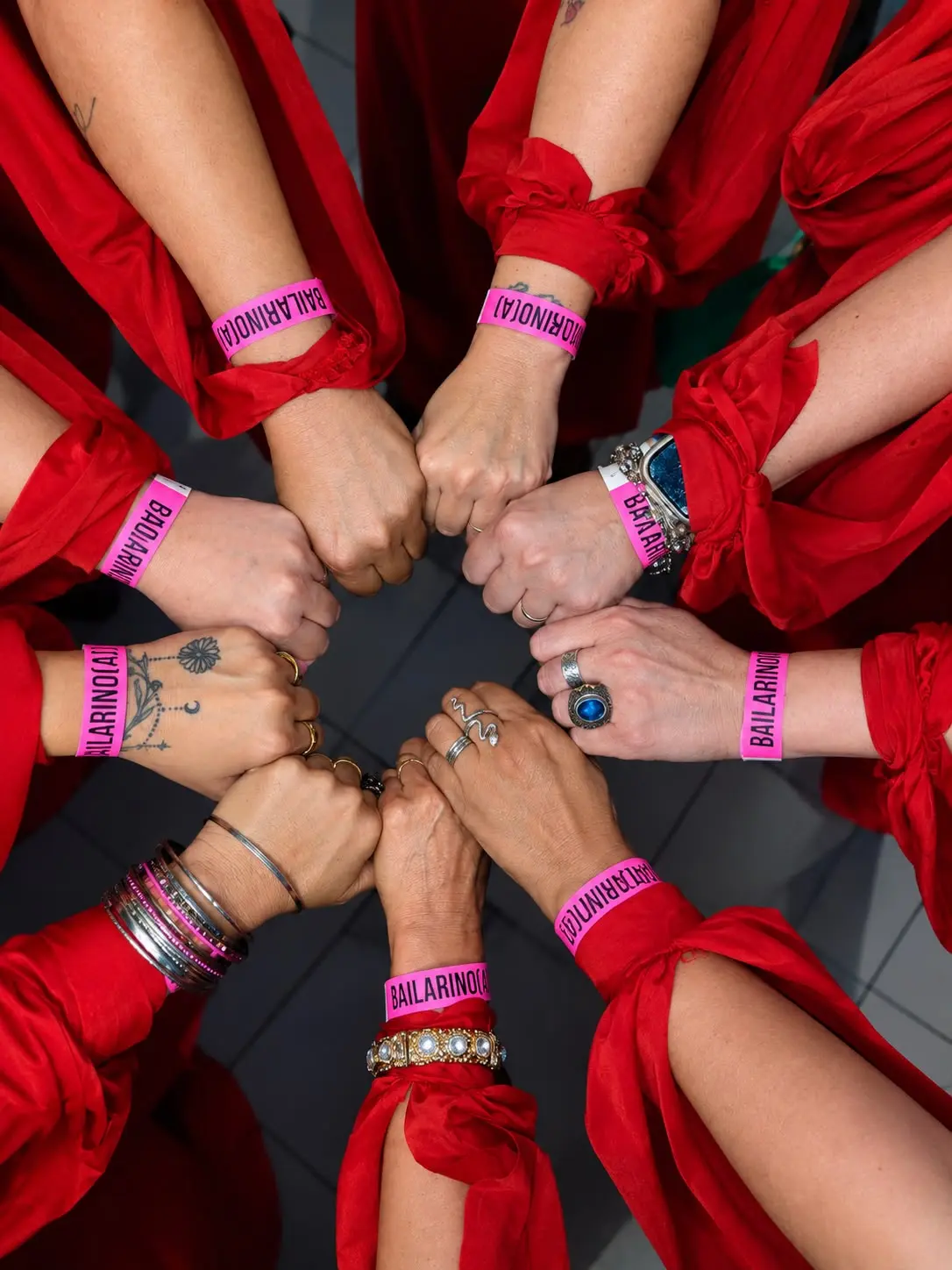 Punhos de bailarinas unidos em círculo, cada um com a pulseira rosa de identificação do festival