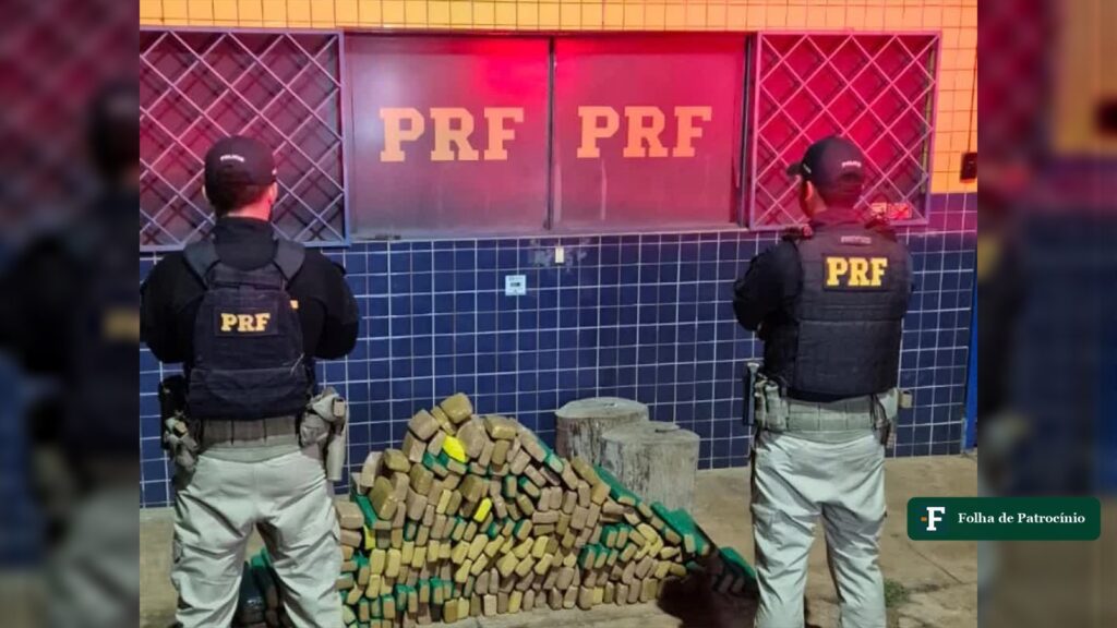 Dois policiais rodoviários federais ao lado de tabletes de maconha empilhados, parte dos 194 kg de maconha apreendidos em Patos de Minas. Foto: PRF/Divulgação