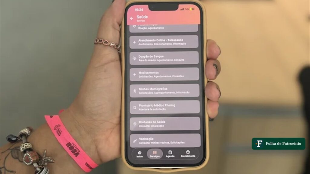 Tela do aplicativo MGApp com a opção Minhas Mamografias no menu Saúde, em celular segurado por uma mulher no Outubro Rosa