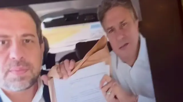 Foto de Camilo Santana e Guilherme Boulos com maço de papel, exibida na tela durante o vídeo sobre os documentos de Lula no TSE