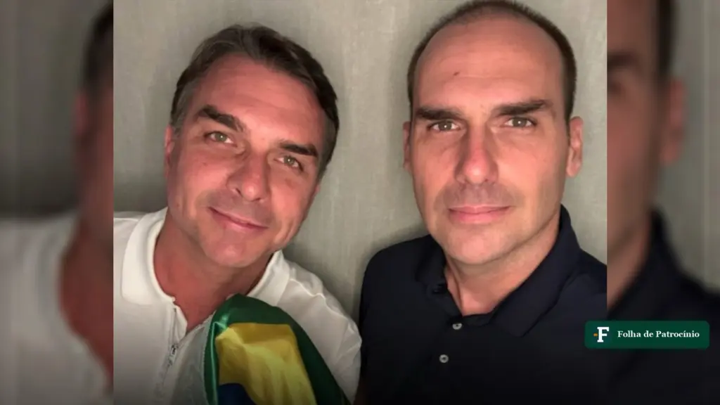 Eduardo Bolsonaro e Flávio posam lado a lado em foto de perto, com uma bandeira do Brasil