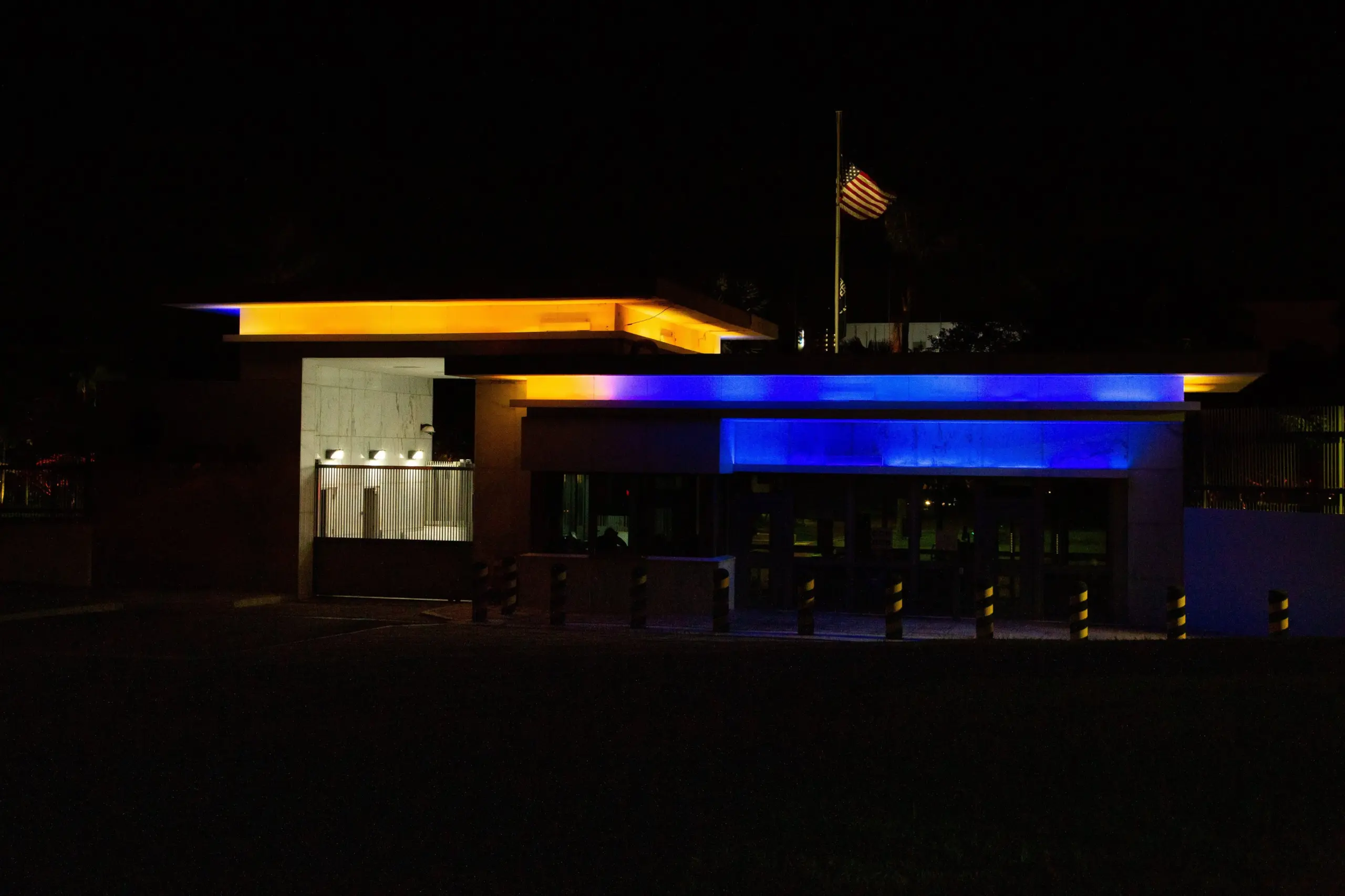 Fachada da Embaixada dos EUA em Brasília à noite, com a bandeira americana no mastro