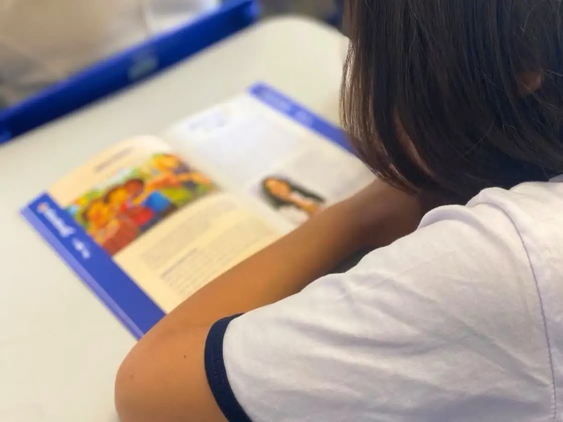 Aluno do 4º ano lê o livreto do Emprega+ nas escolas em sala de aula de Patrocínio