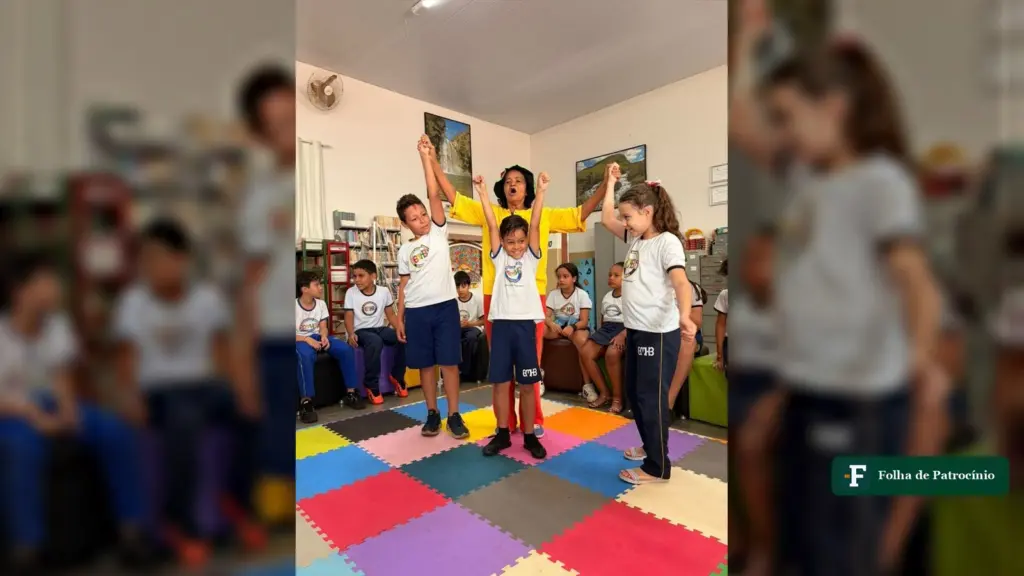 Escola Honorato Borges: crianças de braços erguidos em roda sobre tatame colorido na biblioteca