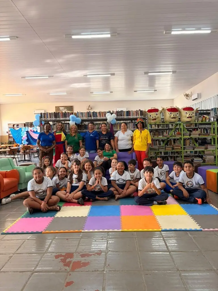 Escola Honorato Borges: alunos sentados e em pé entre as estantes da Biblioteca Pública Municipal