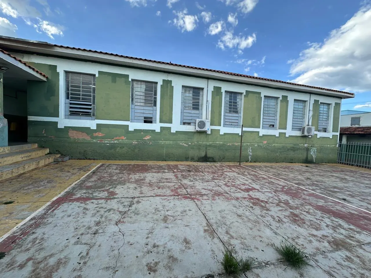 Pátio e quadra da Escola Padre João Balker com piso desgastado e janelas antigas com grades na lateral do prédio