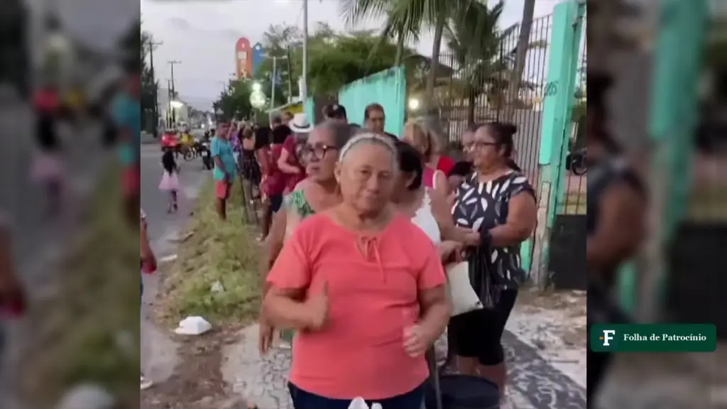Mulher de blusa coral à frente da fila por ossada em Fortaleza, na calçada de uma avenida