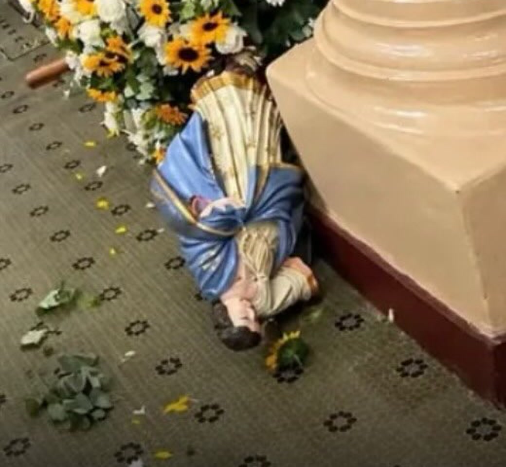 Detalhe da imagem de Nossa Senhora caída no chão da igreja, ao lado do andor decorado com girassóis