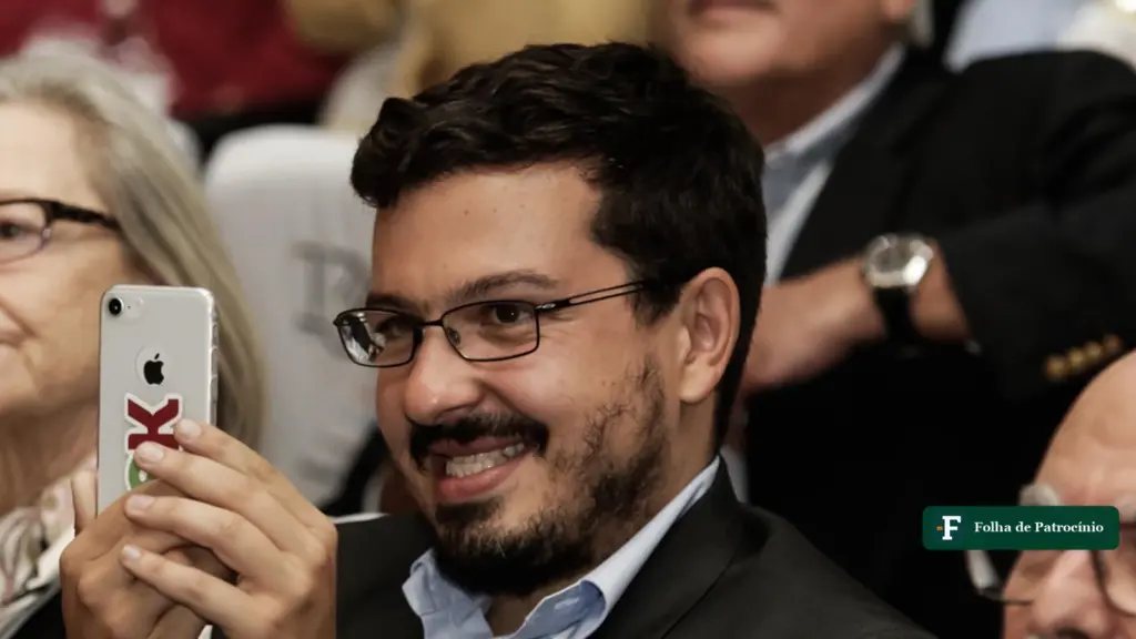 Retrato do jornalista Guilherme Amado sorrindo e segurando o celular, em evento de jornalismo investigativo