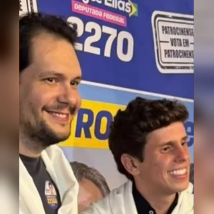 Gustavo Brasileiro e Pedro Bom Negócio sorrindo diante de painel de campanha, na foto que acompanhava o vídeo da carreata de Pedro Bom Negócio