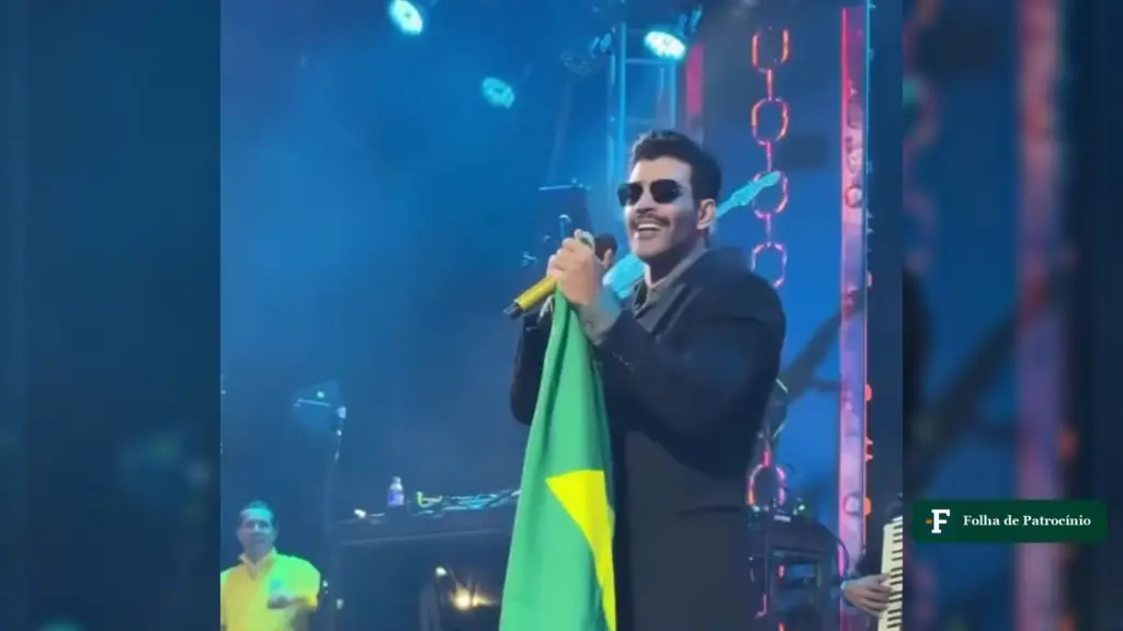 Gusttavo Lima segura bandeira do Brasil no palco, cena ligada a Gusttavo Lima e Flávio
