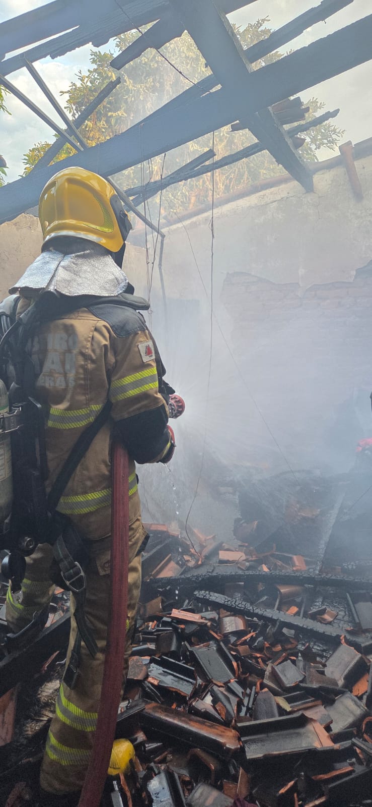Bombeiro militar com mangueira em casa atingida por incêndio em Guimarânia