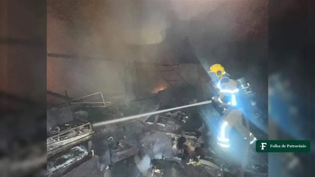 Bombeiro combate com mangueira o incêndio em Patos de Minas que atingiu casa e oficina de estofados