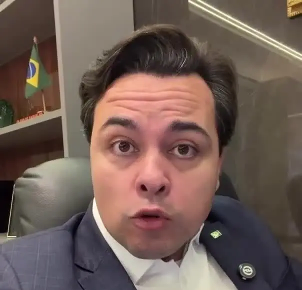 Jeffrey Chiquini grava vídeo sobre os inquéritos do Master e INSS em um escritório com a bandeira do Brasil