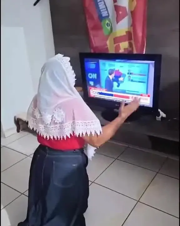 Irmã Mônica ajoelhada diante da televisão com a apuração, em vídeo que ela publicou
