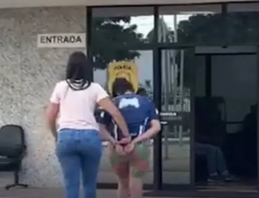 Policial conduz a mãe presa em Brazlândia, algemada, para dentro de uma delegacia