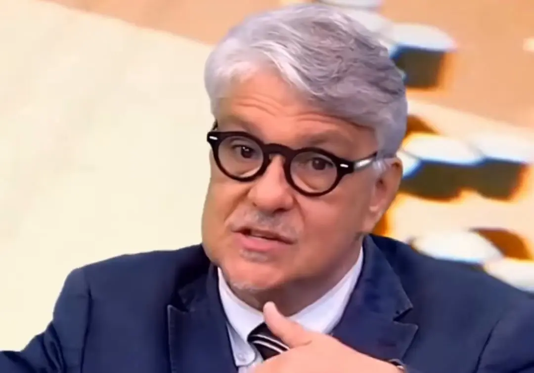 Marcelo Suano falando em entrevista, de óculos redondos e paletó azul