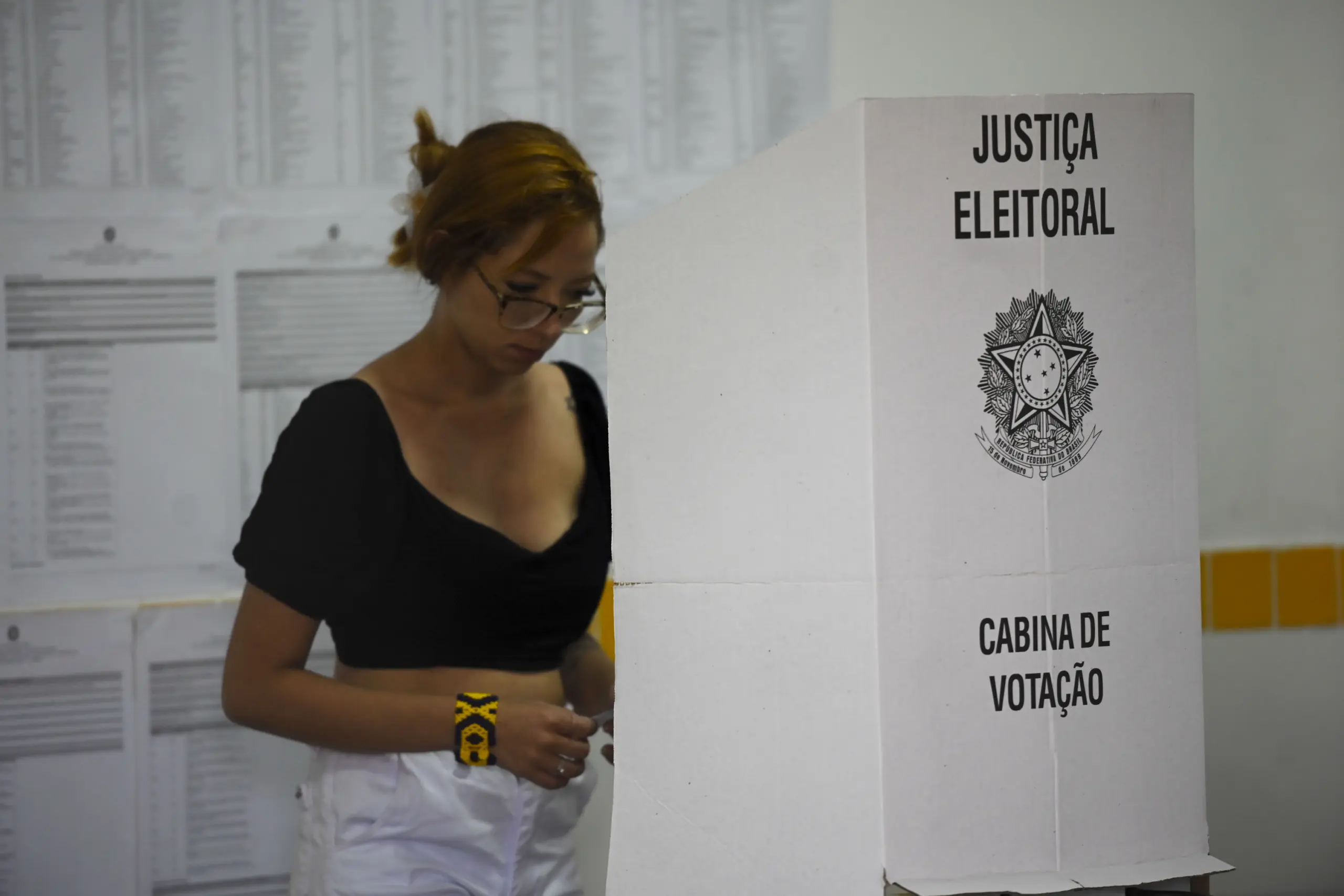 Eleitora ao lado da cabine de votação da Justiça Eleitoral, tema da mudança de local de votação