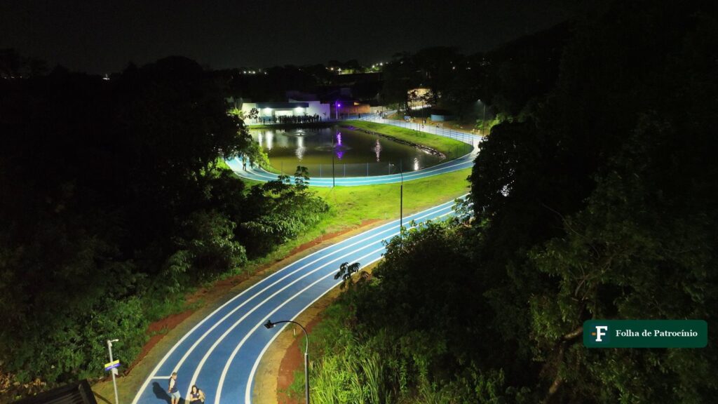 Vista aérea noturna do Parque da Matinha com a pista de caminhada azul iluminada e a lagoa cercada
