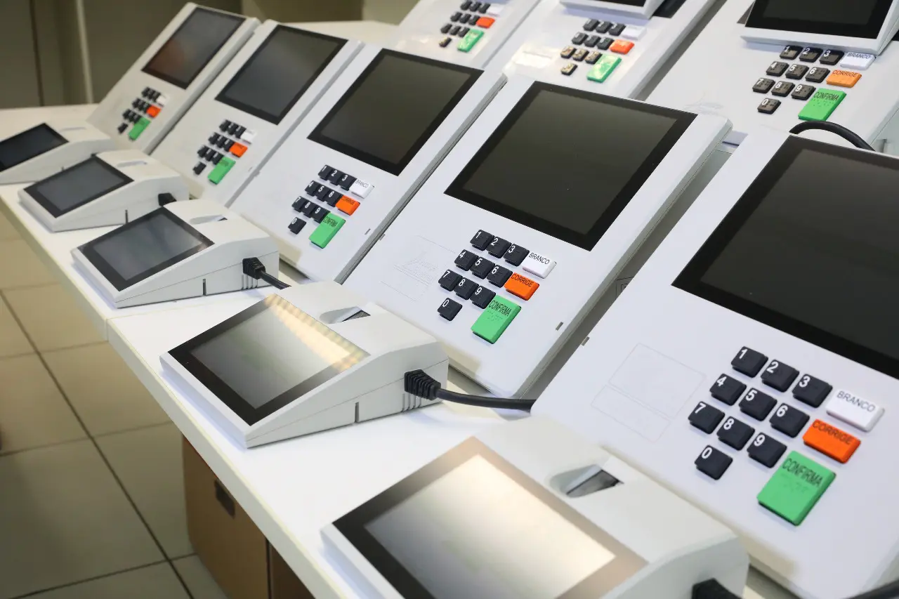 Urnas eletrônicas alinhadas em bancada do TSE, referência para comparar pesquisas e urna