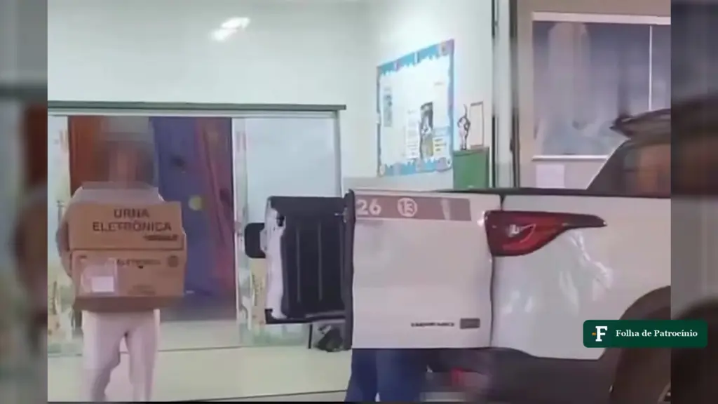 Urnas em caminhonete: mulher carrega caixas de urna eletrônica até uma caminhonete branca com os números 26 e 13 na tampa